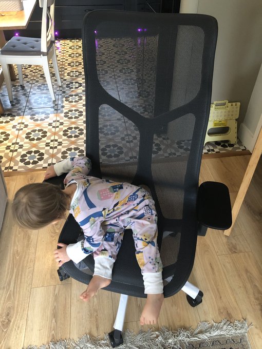 A toddler clambering over a Herman Miller Cosm office chair tipped onto its back.