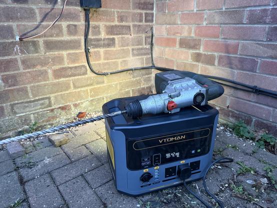 A cordless drill fitted with a very long bit, balanced on top of a VTOMAN portable power station.