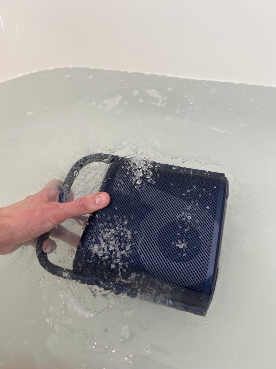 A Soundcore portable speaker being sprayed with water from a garden hose.